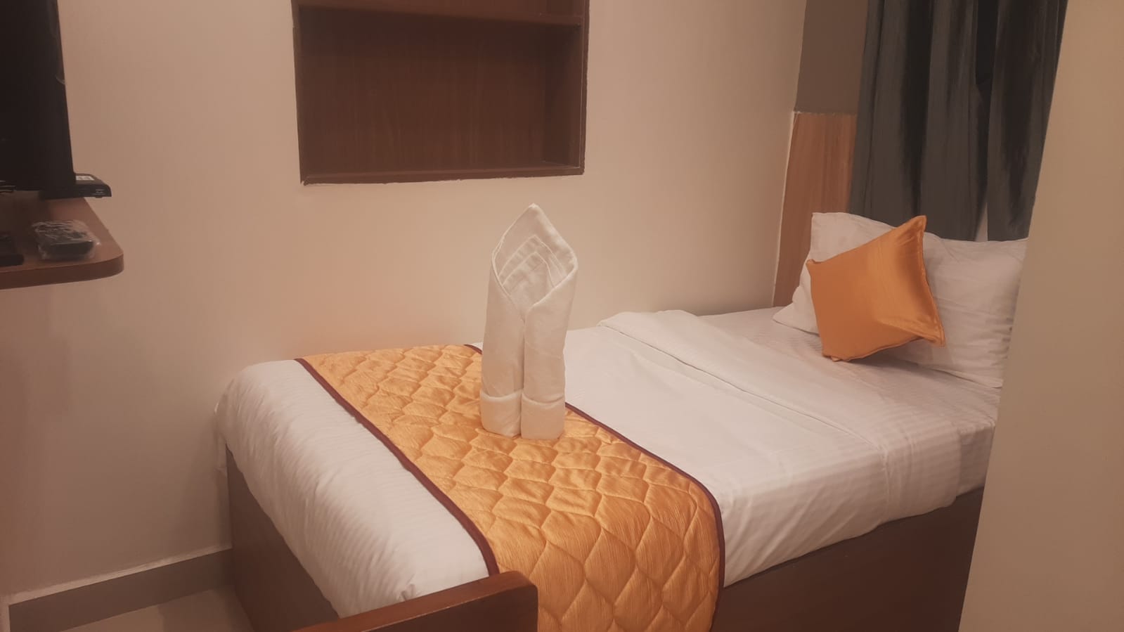 Single bed room with orange runner and a folded towel arrangement
