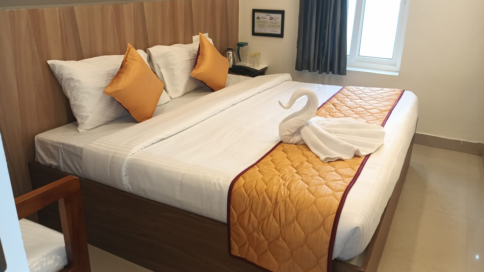 Deluxe room with white linens, warm orange accents, and a swan towel arrangement